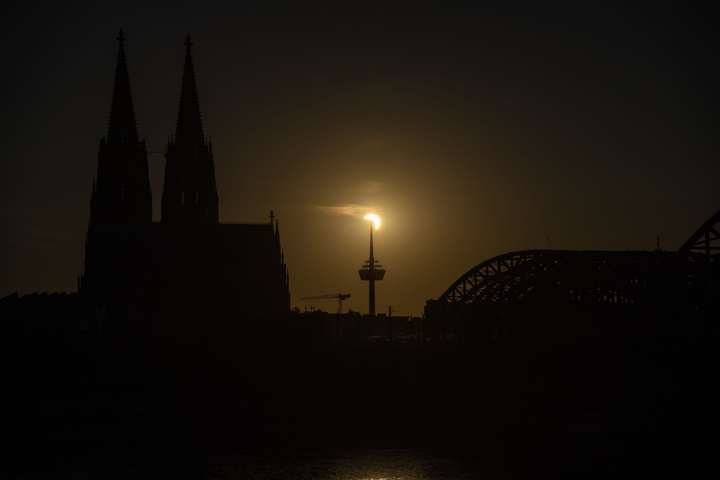Die teilweise durch den Mond verdeckte Sonne an der Spitze des Fernsehturms "Colonius" in der Kölner Skyline mit Dom und Hohenzollern-Brücke