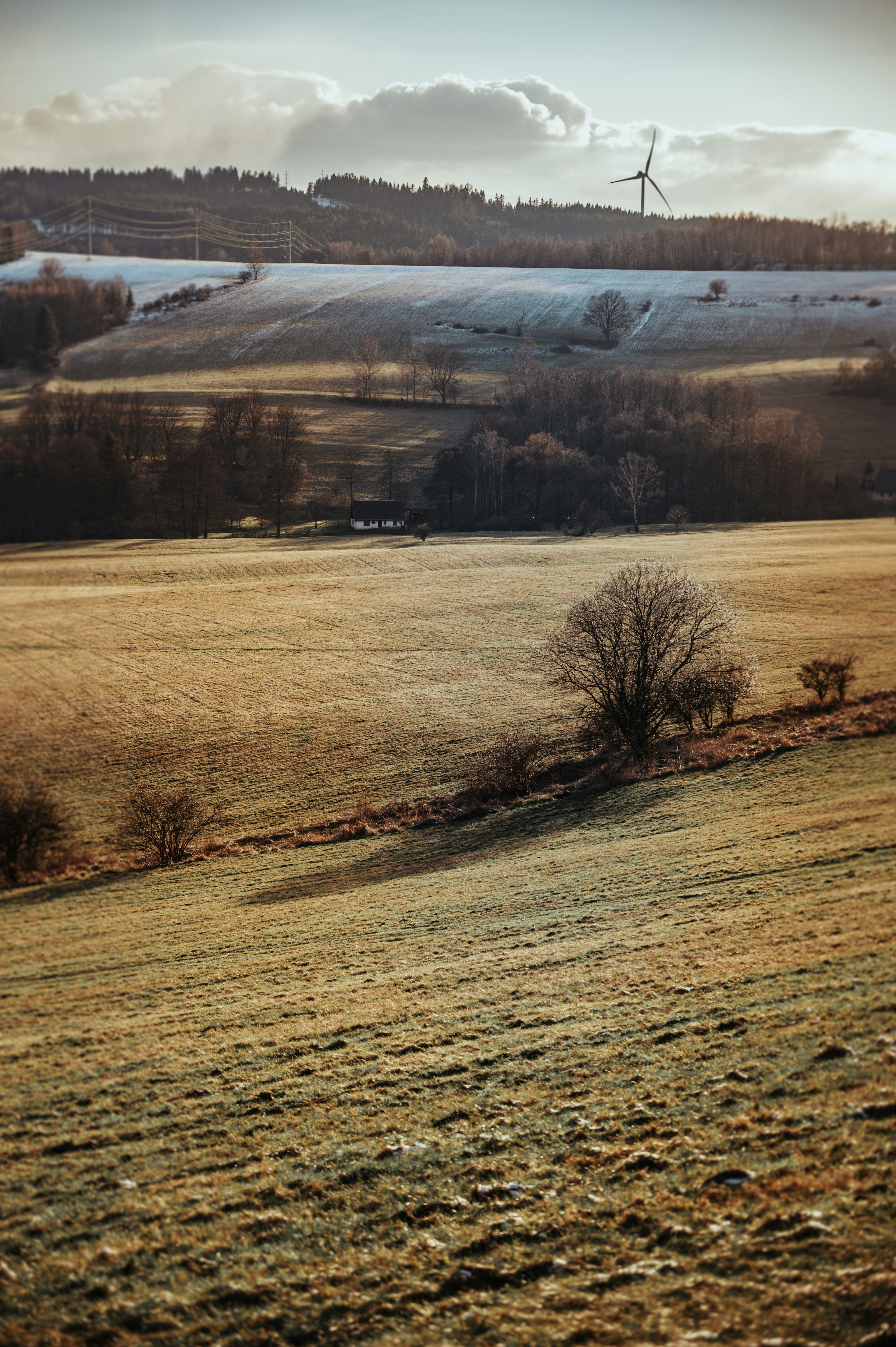 Feld im Sonnenschein mit tauendem Schnee und Windrad am Horizont
